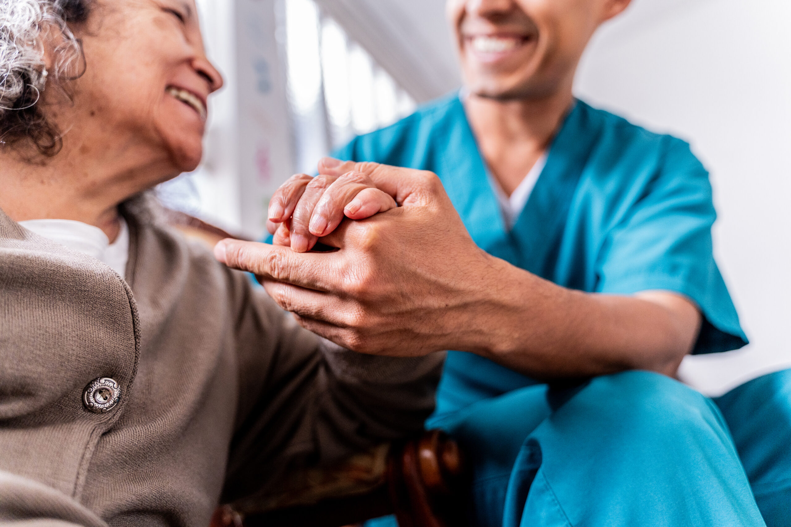 Caregiver holds an older adult’s hands while checking in about new symptoms at home.